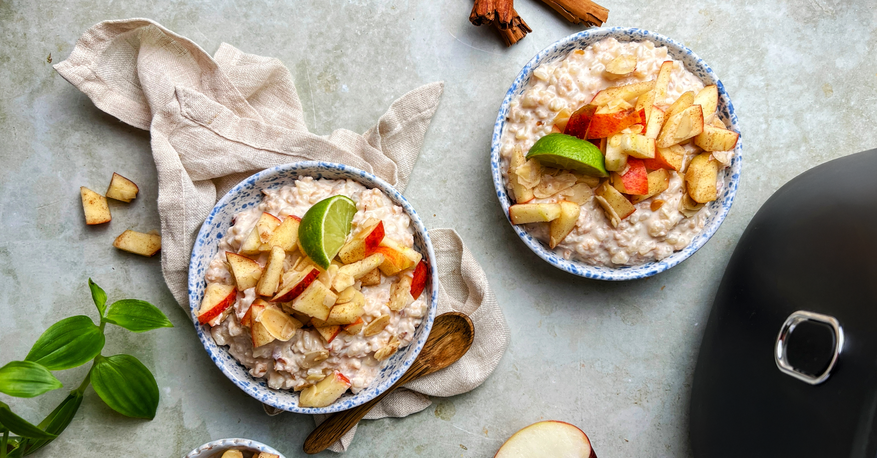 Schüsseln mit cremigem Porridge und Apfelstücken auf heller Fläche, daneben Tuch und Küchenutensilien.